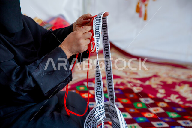 الأصالة والتراث في المملكة العربية السعودية, حرفة يدوية قديمة تاريخية, مهنة شعبية تقليدية, منتج صناعي محلي وطني، صورة مقربة لامرأة عربية خليجية سعودية ترتدي العباءة السوداء تقوم بحياكة الخيوط