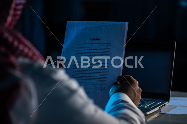 صورة مقربة لرجل عربي خليجي سعودي يحمل بيده ورقة العرض الفني الخاصة بالعمل ،مواصفات المشروع ، المعدات اللازمة ومتطلبات الشركة ،مفهوم التوظيف والعمل