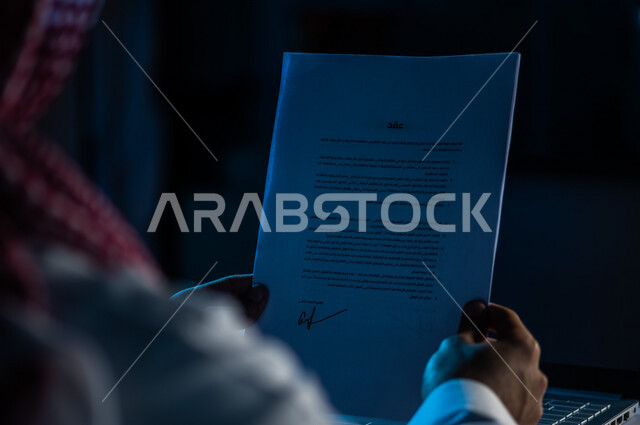 صورة مقربة لرجل عربي خليجي سعودي يحمل بيده ورقة عقد العمل ،وثيقة التوظيف ، قراءة شروط عقد العمل ، الموافقة على العمل ، مفهوم التوظيف والعمل