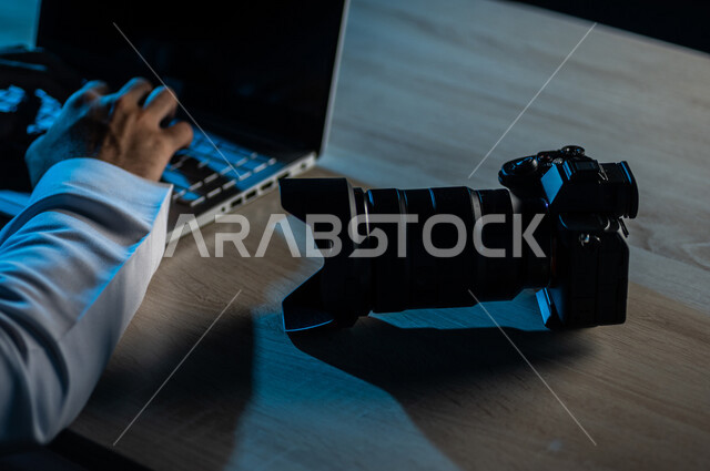 Close-up of a Saudi Arabian Gulf man using his laptop next to his camera, a professional photographer who edits photos, montages and edits videos, photography