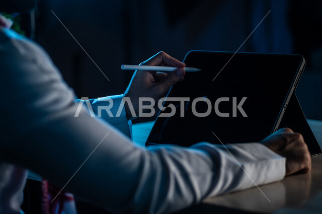 صورة مقربة ليد رجل عربي خليجي سعودي يستخدم جهاز التابلت ، استخدام قلم التابلت لتدوين ملاحظات خاصة بالعمل ،شرح خطوات العمل ، دورات الكترونية ،اعمال ادارية ، التسويق لموقع الكتروني ،رسم الصور والتصاميم