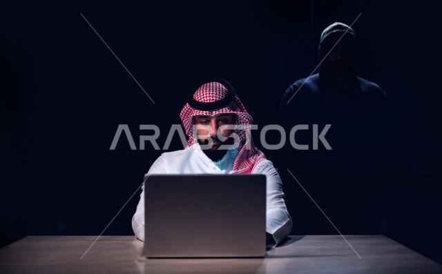 رجل عربي خليجي سعودي يستخدم حاسوبه المحمول، التعرض للإختراق والهجمات الالكترونية، الاختراق الأمني، اختراق حماية وأمن وخصوصية المستخدمين، الجرائم الالكترونية