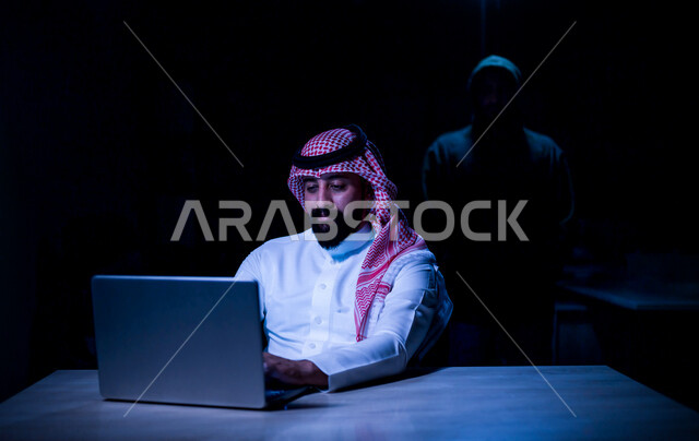رجل عربي خليجي سعودي يستخدم حاسوبه المحمول، التعرض للإختراق والهجمات الالكترونية، الاختراق الأمني، اختراق حماية وأمن وخصوصية المستخدمين، الجرائم الالكترونية