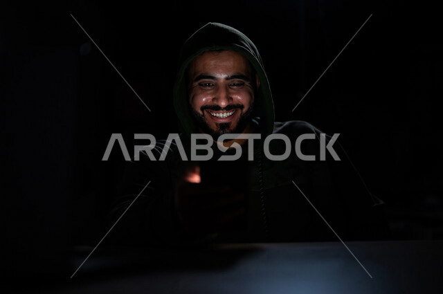 A young Saudi Arabian Gulf man with happy face gestures, working in the field of illegal hacking, penetrating the protection, security and privacy of users, electronic crimes