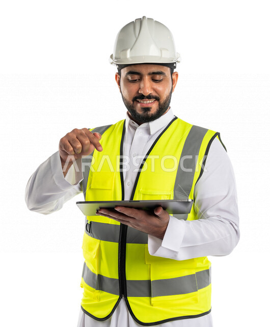 بورتريه لمهندس عربي خليجي سعودي يرتدي الخوذة والسترة الخاصة بالعمل ، يستخدم جهاز التابلت اثناء العمل ،النقر على الشاشة باصبع السبابة ،رسم المخططات ،كتابة وتحديد شيء ما ،تصفح المشاريع ،خلفية بيضاء