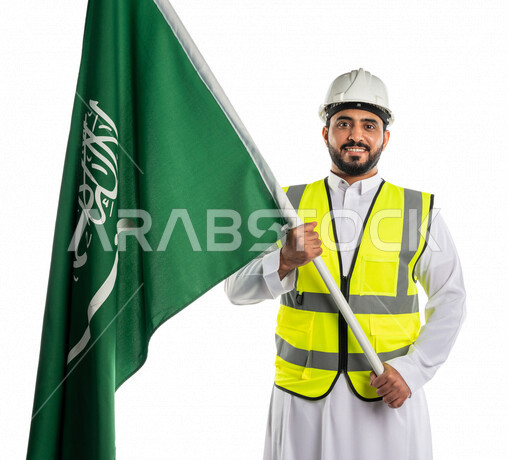 بورتريه لمهندس عربي خليجي سعودي مبتسم وسعيد يرتدي قبعة و سترة الوقاية ، يحمل بيده علم المملكة العربية السعودية ، الاحتفال باليوم الوطني السعودي ،العيد الوطني السعودي ، خلفية بيضاء