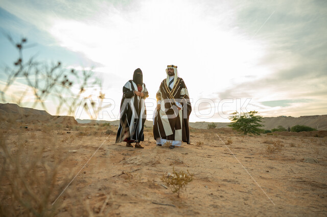 ذكرى تأسيس الدولة السعودية الأولى 1727م, حب الوطن والإنتماء اليه, ارتداء الزي الشعبي في مناسبة وطنية, يوم بدينا 22 فبراير, رجل عربي خليجي سعودي يرتدي البشت والعقال الذهبي وامرأة ترتدي العباءة والبرقع يسيران على الرمال الذهبية في الصحراء