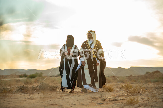 ذكرى تأسيس الدولة السعودية الأولى 1727م, يوم بدينا 22 فبراير, ارتداء الزي الشعبي في مناسبة وطنية, رجل عربي خليجي سعودي يرتدي البشت والعقال الذهبي وامرأة ترتدي العباءة والبرقع يسيران على الرمال الذهبية في الصحراء, الفخر والاعتزاز بالإنتماء الى الوطن