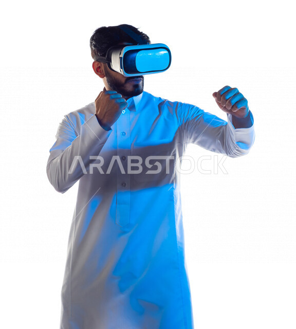 بورتريه لرجل عربي خليجي سعودي يرتدي نظارة الواقع الإفتراضي ثلاثية الأبعاد الفريدة ، يتفاعل بيديه بألعاب الفنون القتالية الدفاعية ، ألعاب العالم الافتراضي ، محاكاة العالم الإفتراضي ، تقنيات و ألعاب ، خلفية بيضاء