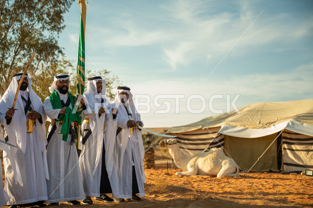 الاحتفال باليوم الوطني بالرقص بالسيوف وقرع الطبول، يوم بدينا ٢٢ فبراير، فرقة عروض الفلكلور التراثي في صحراء المملكة، ارتداء زي العرضة النجدية الشعبية في المناسبة الوطنية، جمل يجلس امام الخيمة، مفهوم حب الوطن والانتماء اليه، ذكرى تاسيس الدوله السعوديه الاولى ١٧٢٧ م