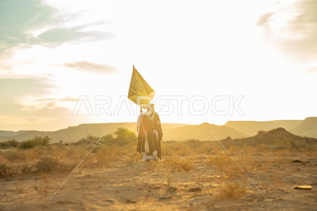 ارتداء زي المنطقة الوسطى, الاحتفال بمناسبة وطنية متميزة, ذكرى تأسيس الدولة السعودية الأولى 1727م, يوم بدينا 22 فبراير, رجل عربي خليجي سعودي يرتدي البشت والعقال الذهبي يرفع سارية لعلم المملكة في الصحراء, مفهوم حب الوطن والانتماء اليه