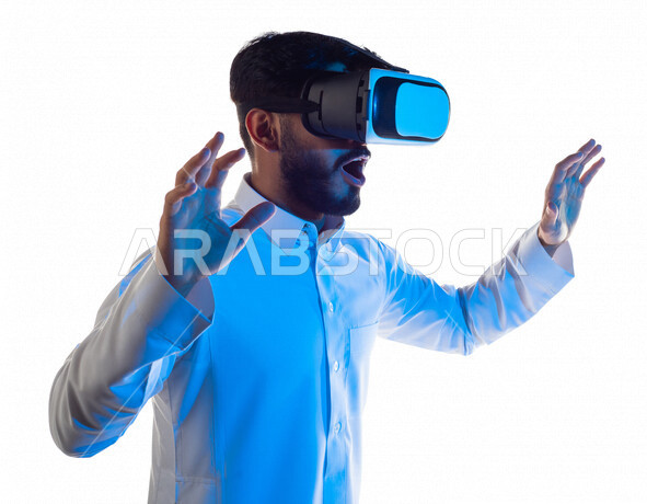 Portrait of a Saudi Arabian Gulf man wearing unique 3D virtual reality glasses, raising the palm of his hands up in amazement, interaction and entertainment by watching movies and virtual world games, simulation of the virtual world, white background