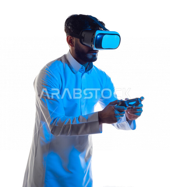بورتريه لرجل عربي خليجي سعودي يرتدي نظارة الواقع الإفتراضي ثلاثية الأبعاد ، يمسك بيده عصا التحكم و يلعب بألعاب الفيديو بإيماءات تدل على التركيز ،  المتعة و التسلية بألعاب العالم الافتراضي ، ألعاب البلايستيشن الترفيهية ، تقنيات و ألعاب