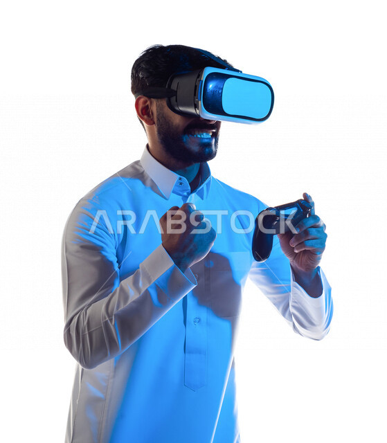 بورتريه لرجل عربي خليجي سعودي يرتدي نظارة الواقع الإفتراضي ثلاثية الأبعاد ، يمسك بيده عصا التحكم و يلعب بألعاب الفيديو بإيماءات تدل على الفوز ،  المتعة و التسلية بألعاب العالم الافتراضي ، ألعاب البلايستيشن الترفيهية ، تقنيات و ألعاب