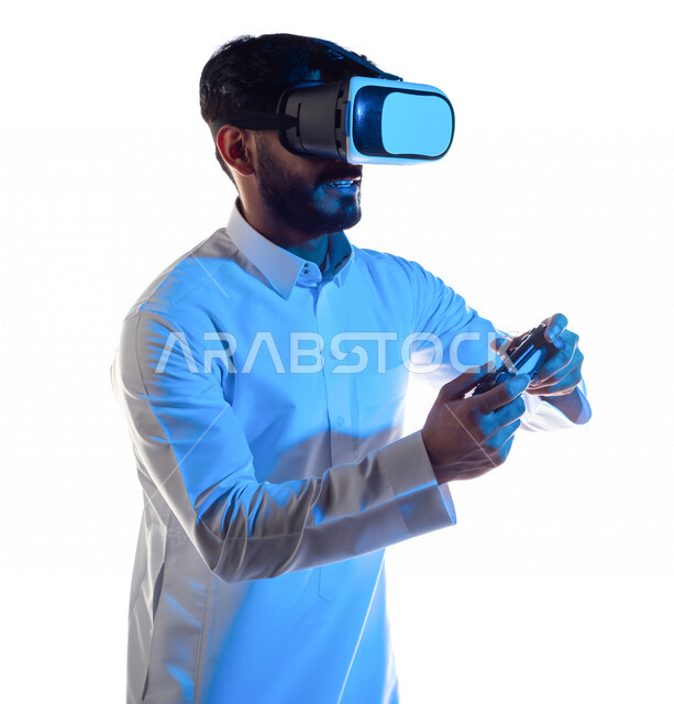 Portrait of a Saudi Arabian Gulf man wearing 3D virtual reality glasses, holding a joystick in his hand and playing video games with gestures that indicate focus, fun and entertainment in virtual world games, PlayStation entertainment games, techniques an