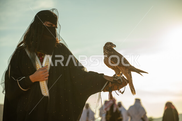 مكانة الصقور في التاريخ السعودي, تربية الطائر الجارح، ذكرى تاسيس الدوله السعوديه الاولى 1727م, يوم بدينا 22 فبراير، مفهوم الافتراس وحدة البصر, امرأة عربية خليجية سعودية ترتدي البشت النسائي السعودي و البرقع يقف على يدها الصقر, خلفية العرضة النجدية في الصحراء