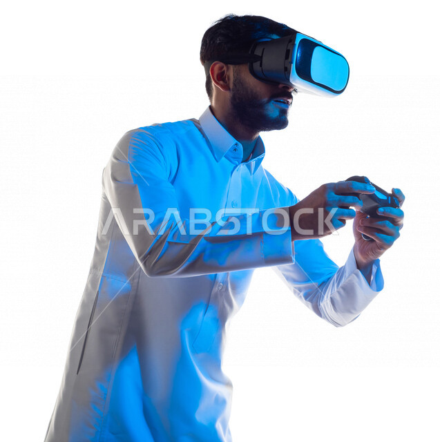 بورتريه لرجل عربي خليجي سعودي يرتدي نظارة الواقع الإفتراضي ثلاثية الأبعاد ، يمسك بيده عصا التحكم و يلعب بألعاب الفيديو بإيماءات تدل على التركيز ،  المتعة و التسلية بألعاب العالم الافتراضي ، ألعاب البلايستيشن الترفيهية ، تقنيات و ألعاب