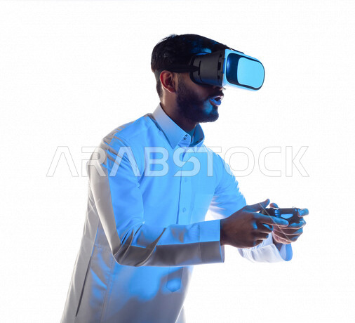 بورتريه لرجل عربي خليجي سعودي يرتدي نظارة الواقع الإفتراضي ثلاثية الأبعاد ، يمسك بيده عصا التحكم و يلعب بألعاب الفيديو بإيماءات تدل على التركيز ،  المتعة و التسلية بألعاب العالم الافتراضي ، ألعاب البلايستيشن الترفيهية ، تقنيات و ألعاب