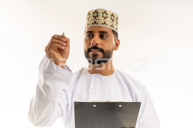 Daily task writing tools, recording important notes and information, close-up portrait of an Arab Gulf Omani man wearing a dishdasha and a kummah holding a black paper holder and a pen in his hands, looking at it with gestures of concentration and contemplation, white background