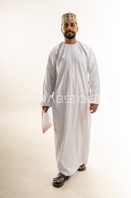 إيماءات المشي والذهاب إلى مكان معين، دراسة جدوى العمل، مراجعة نتيجة الاجتماع، بورتريه لرجل عربي خليجي عماني يرتدي الدشداشة والكمة يحمل بيده ملف ينظر إلى الكاميرا بتعابير الجدية والثقة، إعداد التقرير اليومي، الجسم بالطول الكامل، خلفيه بيضاء