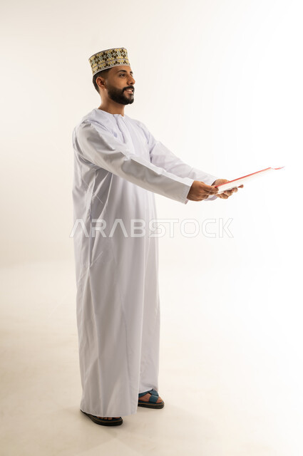 تدوين الملاحظات وإعداد التقرير اليومي، دراسة جدوى العمل، مراجعة نتيجة الاجتماع، بورتريه لرجل عربي خليجي عماني يرتدي الدشداشة والكمة يحمل بيديه ملف يقوم بتقديمه إلى شخص ما ينظر إلى مكان معين بإيماءات الجدية والثقة، الجسم بالطول الكامل، خلفيه بيضاء