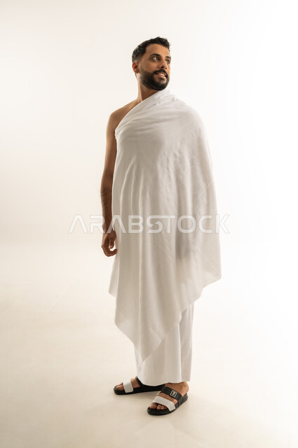العبادة والطاعة والتقرب إلى الله, أداء مناسك الحج والعمرة، بورتريه من الجانب لرجل عربي عماني خليجي يرتدي ملابس الإحرام ينظر إلى مكان ما بعيد بإيماءات التأمل والشرود، الجسم بالطول الكامل، خلفية بيضاء