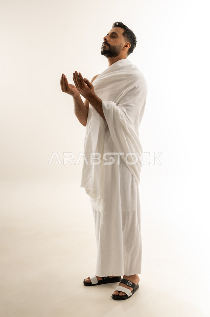 الدعاء بخضوع ورفع الكفين نحو الأعلى، العبادة والطاعة والإكثار من الأذكار, طلب العفو والمغفرة من الله تعالى، أداء مناسك الحج والعمرة، بورتريه من الجانب لرجل عربي عماني خليجي يرتدي ملابس الإحرام يدعو الله بخشوع وتذلل، الجسم بالطول الكامل، خلفية بيضاء
