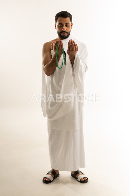 طلب العفو والمغفرة من الله تعالى، رفع الكفين نحو الأعلى والدعاء، العبادة والطاعة والإكثار من الأذكار, أداء مناسك الحج والعمرة، بورتريه لرجل عربي عماني خليجي يرتدي ملابس الإحرام يمسك بيده السبحة ويدعو الله، الجسم بالطول الكامل، خلفية بيضاء