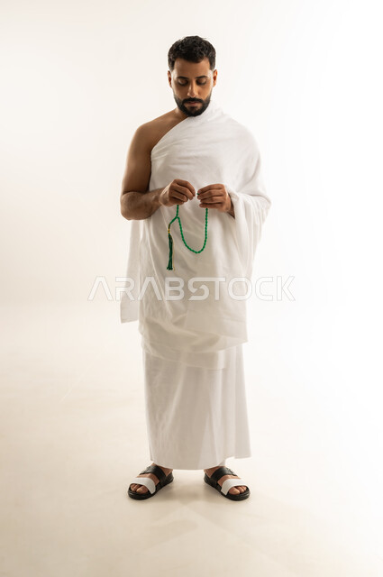 العبادة والطاعة والإكثار من الأذكار, التسبيح والتهليل وطلب العفو والمغفرة من الله تعالى، أداء مناسك الحج والعمرة، بورتريه لرجل عربي عماني خليجي يرتدي ملابس الإحرام يمسك بيده السبحة ويسبح، الجسم بالطول الكامل، خلفية بيضاء
