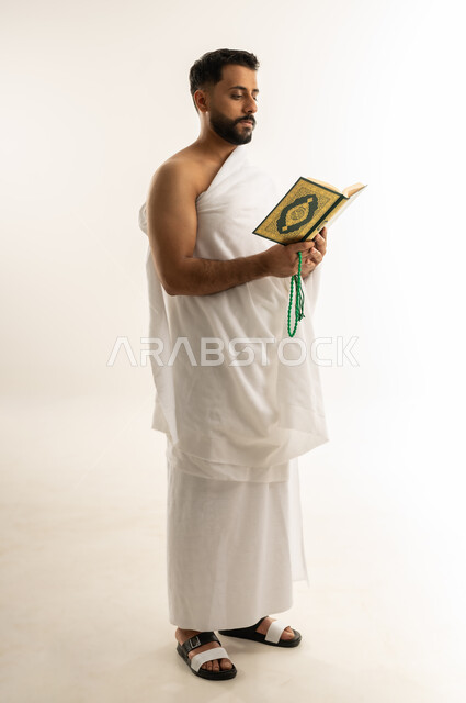 التقرب الى الله بالعبادة والطاعة, أداء مناسك الحج والعمرة، قراءة القرآن الكريم بتمعن وتركيز, تلاوة كتاب الله، بورتريه من الجانب لرجل عربي عماني خليجي يرتدي ملابس الإحرام ويمسك بين يديه المصحف الشريف والسبحة، الجسم بالطول الكامل، خلفية بيضاء
