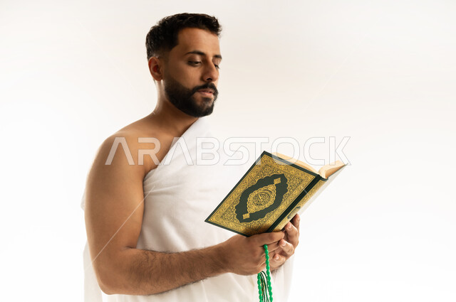 ترتيل وتلاوة كتاب الله، التقرب الى الله بالعبادة والطاعة, أداء مناسك الحج والعمرة، قراءة القرآن الكريم بتمعن وتركيز, بورتريه مقرب من الجانب لرجل عربي عماني خليجي يرتدي ملابس الإحرام ويمسك بين يديه المصحف الشريف والسبحة، خلفية بيضاء