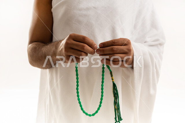 التسبيح والتهليل وذكر الله، التقرب الى الله بالعبادة والطاعة, أداء مناسك الحج والعمرة، بورتريه مقرب لرجل عربي عماني خليجي يرتدي ملابس الإحرام ويمسك السبحة ذات الحبات الخضراء بيده ويسبح عبرها، خلفية بيضاء