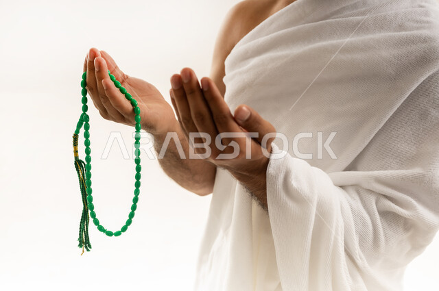 الدعاء بخشوع وخضوع، العبادة والطاعة والتقرب الى الله, التسبيح والتهليل وذكر الله، أداء مناسك الحج والعمرة، بورتريه مقرب من الجانب لرجل عربي عماني خليجي يرتدي ملابس الإحرام ويمسك السبحة بيده ويرفع كفيه نحو الأعلى، خلفية بيضاء