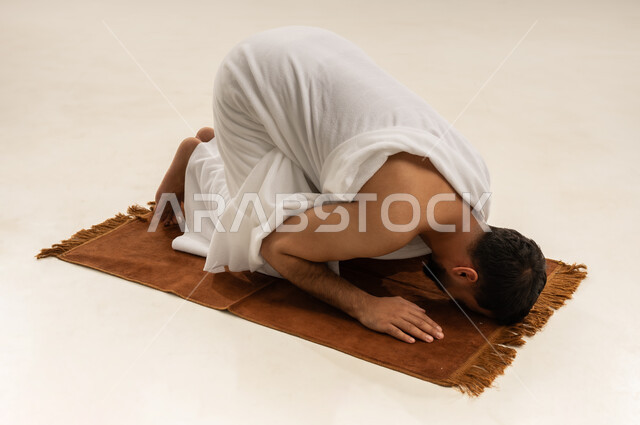 التوجه للقبلة وأداء فريضة الصلاة, بورتريه لرجل عربي عماني خليجي يرتدي ملابس الإحرام ويقوم بالسجود على سجادة الصلاة، مناسك الحج والعمرة، التقرب الى الله بأداء العبادة والطاعة, خلفية بيضاء