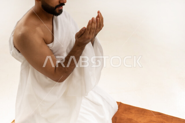 الدعاء بخشوع وتضرع، طلب المغفرة والعفو من الله، بورتريه مقرب لرجل عربي خليجي عماني يرتدي ملابس الإحرام ويرفع كفيه المفتوحتين للأعلى ويدعو، أداء مناسك الحج والعمرة، التقرب إلى الله بالعبادة والطاعة، خلفية بيضاء