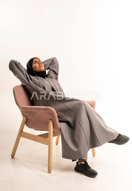 النظر للأعلى إلى شيء ما، إيماءات الراحة والإسترخاء، الشعور بالتعب و الخمول والحاجة إلى النوم, بورتريه لامرأة عربيه خليجيه سعوديه محجبه ترتدي العباءة تجلس على كرسي مريح تضع يديها وراء رأسها بتعابير التأمل والسرور، خلفية بيضاء