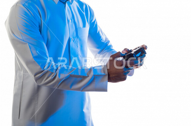 صورة مقربة لرجل عربي خليجي سعودي ، يمسك عصا التحكم و يلعب بألعاب الفيديو ، المتعة و التسلية بألعاب الفيديو و ألعاب العالم الافتراضي ، ألعاب البلايستيشن الترفيهية ، تقنيات و ألعاب ، خلفية بيضاء