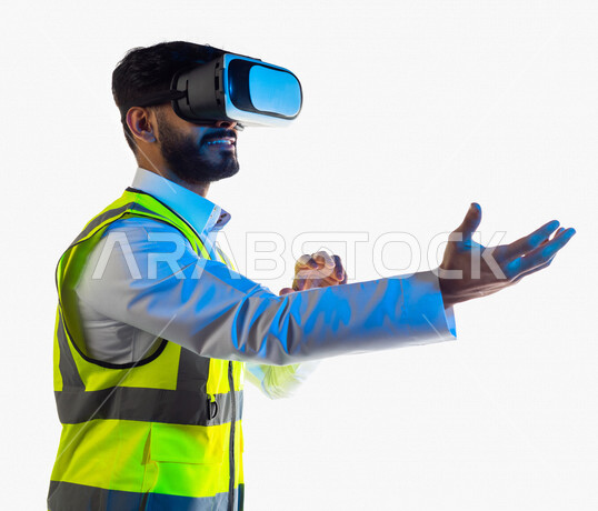 Portrait of an Arab, Gulf, Saudi engineer wearing a work jacket and 3D virtual reality glasses, pointing with his hand towards something he is holding in the other hand in virtual reality, merging virtual reality technology architecture, lifting and carry