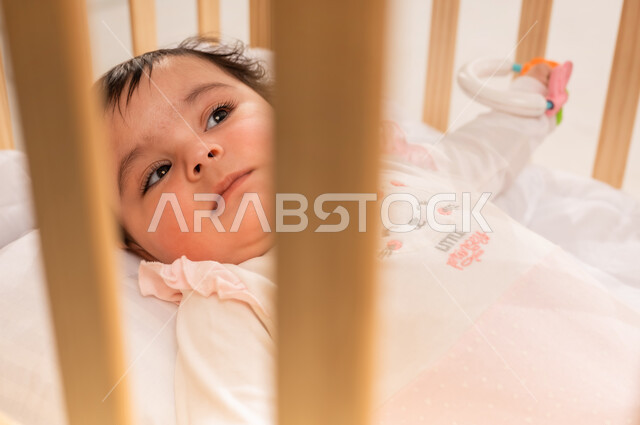 الملامح الطفولية البريئة الناعمة, الاهتمام والاعتناء بمظهر الأطفال الخارجي, مفهوم البراءة والطفولة, صورة مقربة لرضيعة عربية خليجية سعودية ترتدي لباس قطني مريح تستلقي على ظهرها في السرير