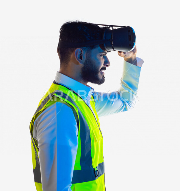 بورتريه لمهندس عربي خليجي سعودي يرتدي سترة خاصة بالعمل و نظارة الواقع الإفتراضي ثلاثية الأبعاد ، إدماج تقنية الواقع الافتراضي في الهندسة المعمارية ، تطبيق تكنولوجيا الواقع الافتراضي ، التخطيط الحَضَرِي ، خلفية بيضاء