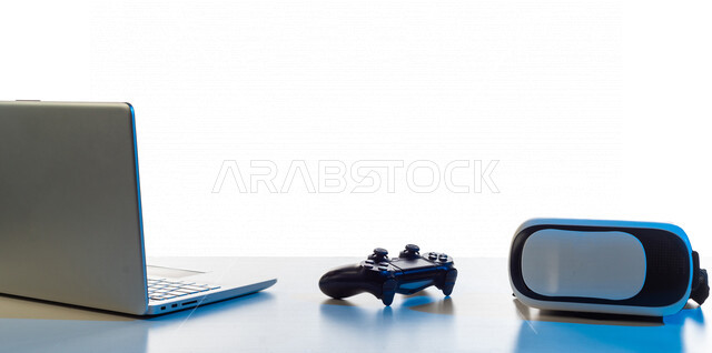 طاولة تحتوى على نظارة واقع افتراضي و عصا التحكم لألعاب الفيديو البلايستيشن ، و جهاز حاسوب محمول ، أجهزة تكنولوجية و الكترونية ، تقنيات و ألعاب ، خلفية بيضاء