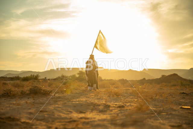 يوم بدينا 22 فبراير, الاحتفال بذكرى تأسيس الدولة السعودية الأولى 1727م, مناسبة وعيد وطني متميز, ارتداء زي المنطقة الوسطى, الفخر والاعتزاز بالانتماء للوطن, رجل عربي خليجي سعودي يرتدي البشت والعقال الذهبي يرفع علم المملكة عند شروق الشمس في الصحراء