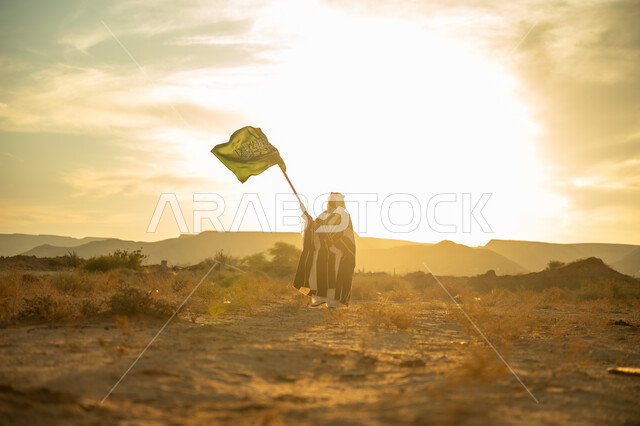 ذكرى تأسيس الدولة السعودية الأولى 1727م, مناسبة وعيد وطني متميز, ارتداء زي المنطقة الوسطى, الفخر والاعتزاز بالانتماء للوطن, يوم بدينا 22 فبراير, رجل عربي خليجي سعودي يرتدي البشت والعقال الذهبي يرفع علم المملكة عند شروق الشمس في الصحراء