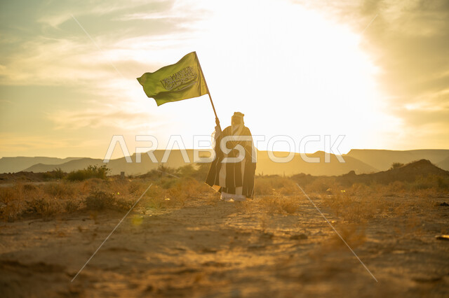 ذكرى تأسيس الدولة السعودية الأولى 1727م, عيد ومناسبة وطنية متميزة, ارتداء زي المنطقة الوسطى, الفخر والاعتزاز بالهوية الوطنية, يوم بدينا 22 فبراير, رجل عربي خليجي سعودي يرتدي البشت والعقال الذهبي يرفع سارية علم المملكة عند شروق الشمس في الصحراء