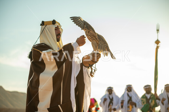 يوم بدينا 22 فبراير، الاهتمام بتربيه الطيور و تدريبها, مكانة الصقور في التاريخ السعودي, ذكرى تاسيس الدوله السعوديه الاولى 1727 م, مناسبة شعبيه وطنيه, رجل عربي خليجي سعودي يرتدي الغترة والبشت يحمل على يده طائر الصقر بتعابير الفخر, خلفية العرضة النجدية