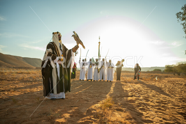ذكرى تاسيس الدوله السعوديه الاولى 1727 م, مناسبة شعبيه وطنيه, يوم بدينا 22 فبراير، الاهتمام بتربية الطيور و تدريبها, مكانة الصقور في التاريخ السعودي, رجل عربي خليجي سعودي يرتدي الغترة والبشت يحمل على يده طائر الصقر بتعابير الفخر, خلفية العرضة النجدية في الصحراء