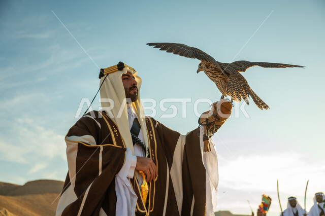 الاهتمام بتربية الطيور و تدريبها, مكانة الصقور في التاريخ السعودي, صورة مقربة لرجل عربي خليجي سعودي يرتدي الغترة والبشت يحمل على يده طائر الصقر, يوم بدينا 22 فبراير، ذكرى تاسيس الدوله السعوديه الاولى 1727 م, مناسبة وطنيه شعبيه, خلفية العرضة النجدية في الصحراء