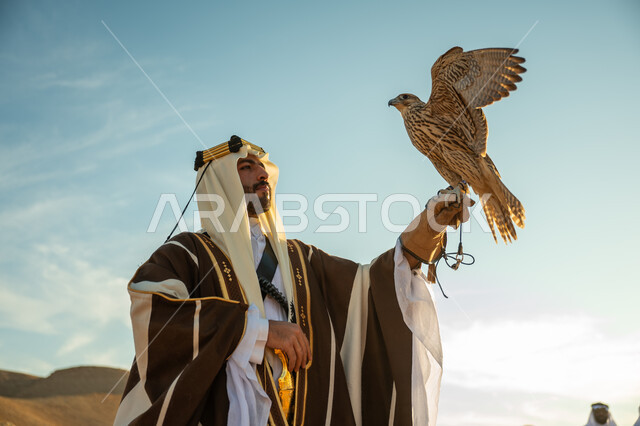 ذكرى تاسيس الدوله السعوديه الاولى 1727 م, يوم بدينا 22 فبراير، العناية بتربية الطيور و تدريبها, مكانة الصقور في التاريخ السعودي, صورة مقربة لرجل عربي خليجي سعودي يرتدي الغترة والبشت يحمل على يده طائر الصقر بتعابير الفخر, مناسبة وطنيه شعبيه