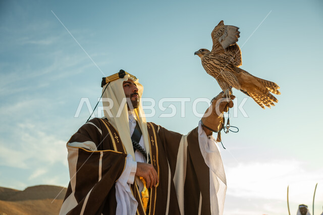ذكرى تاسيس الدوله السعوديه الاولى 1727 م, يوم بدينا 22 فبراير، العناية بتربية الطيور و تدريبها, مكانة الصقور في التاريخ السعودي, صورة مقربة لرجل عربي خليجي سعودي يرتدي الغترة والبشت يحمل على يده طائر الصقر بتعابير الفخر, مناسبة وطنيه شعبيه