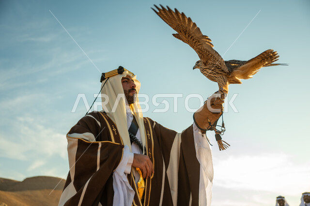 The day we started February 22, caring for raising and training birds, the status of falcons in Saudi history, a close-up of a Saudi Arabian Gulf man wearing a ghutra and a bisht holding a falcon in his hand with expressions of pride, the anniversary of the founding of the first Saudi state 1727 AD, a popular national occasion